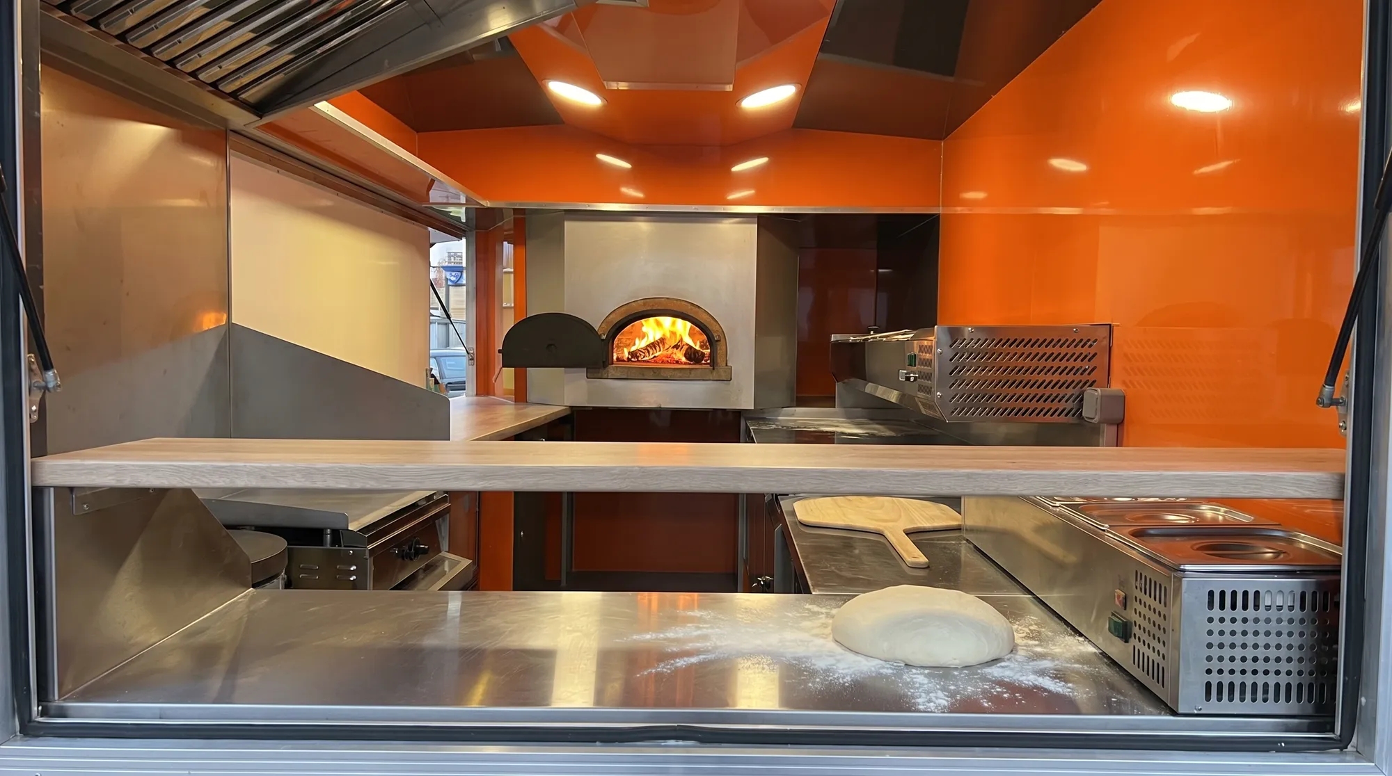 Intérieur du camion pizza avec four à bois en brique et plans de travail inox