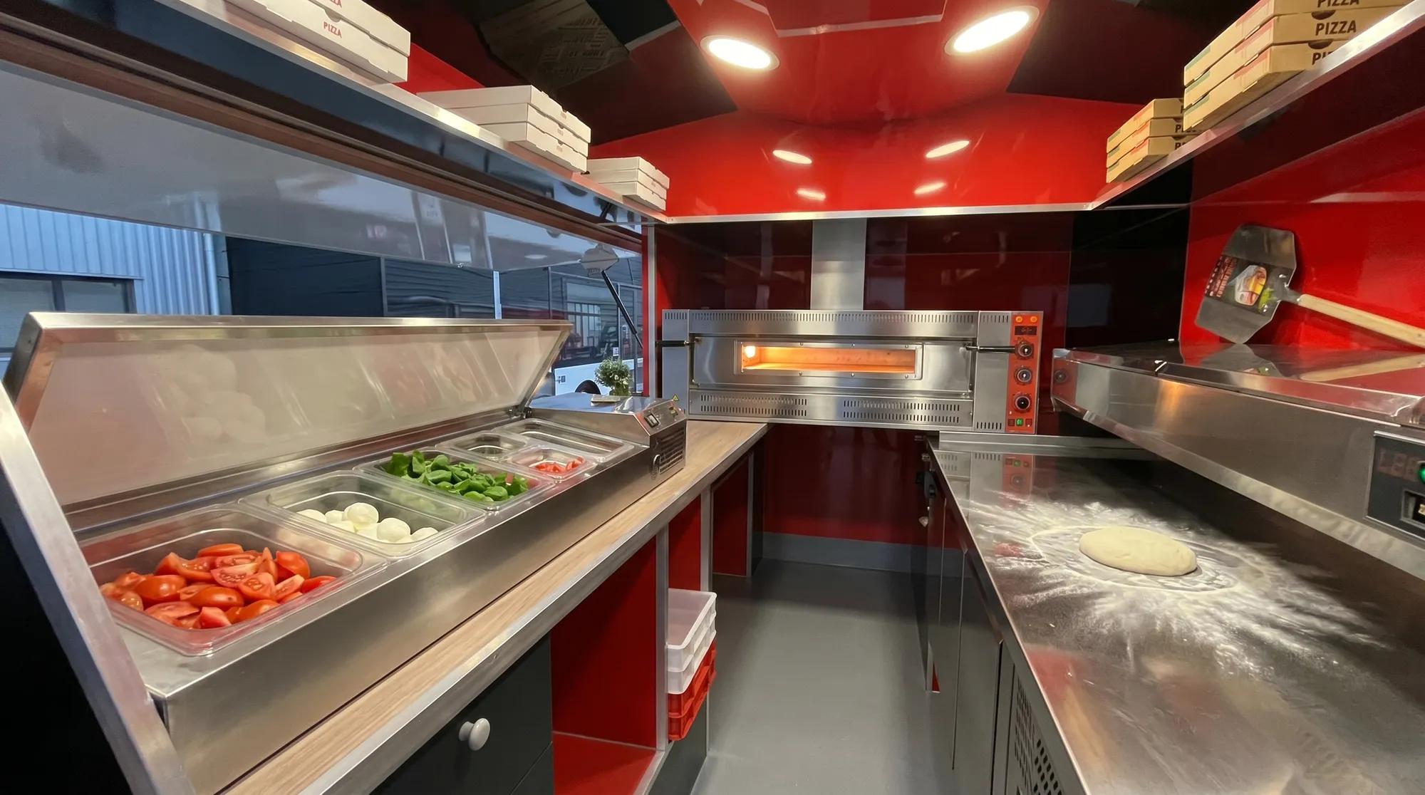 Intérieur rouge du camion pizza avec four à gaz inox et saladette à garnitures